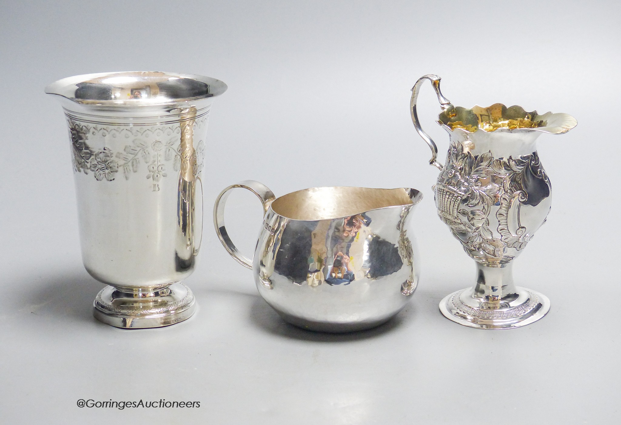 A George III later embossed silver cream jug with later base?, 11.5cm, a modern silver cream jug and a French white metal beaker, gross 10.5oz.